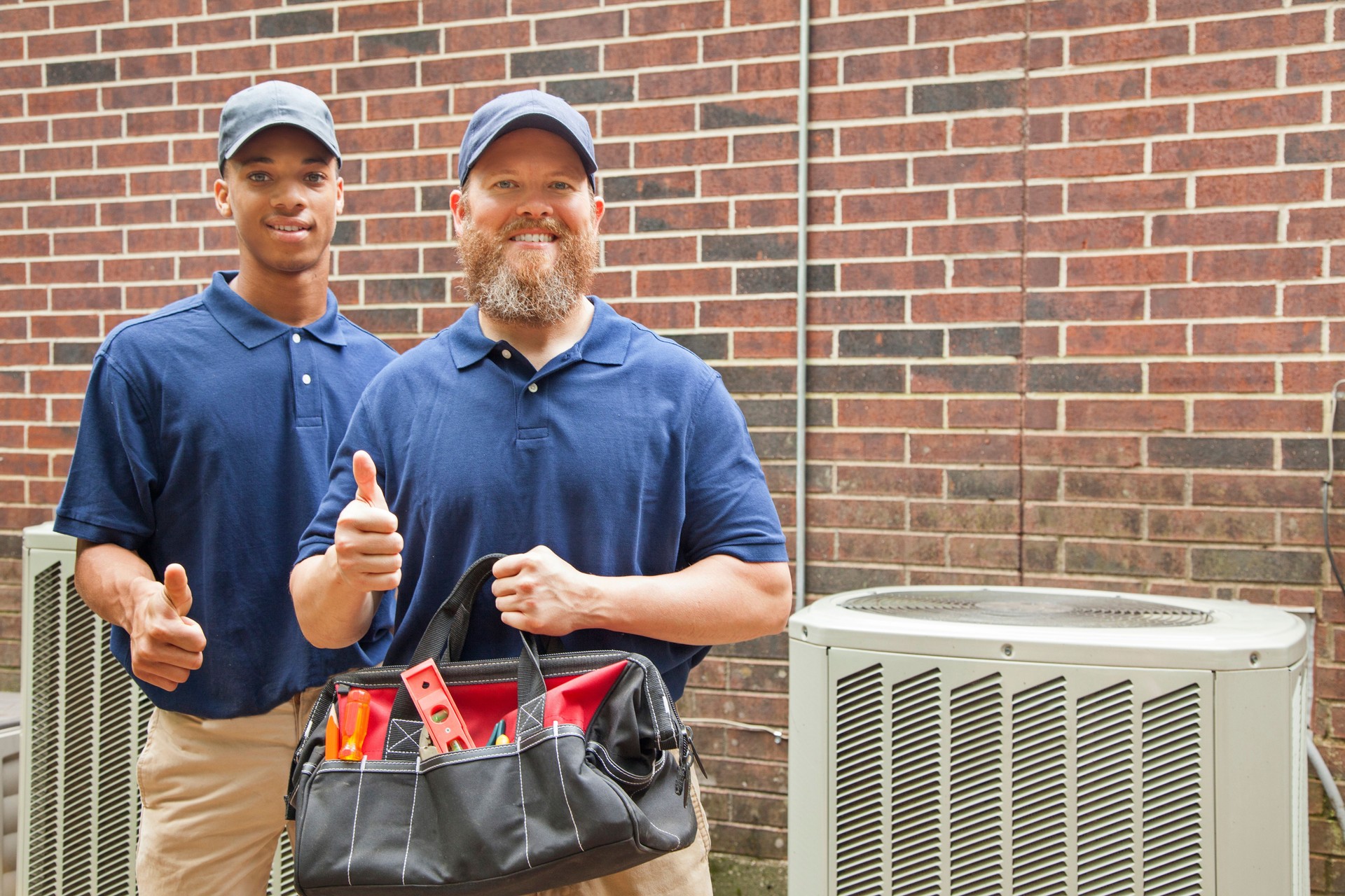 Air conditioner repairmen work on home unit.  Tool bag.